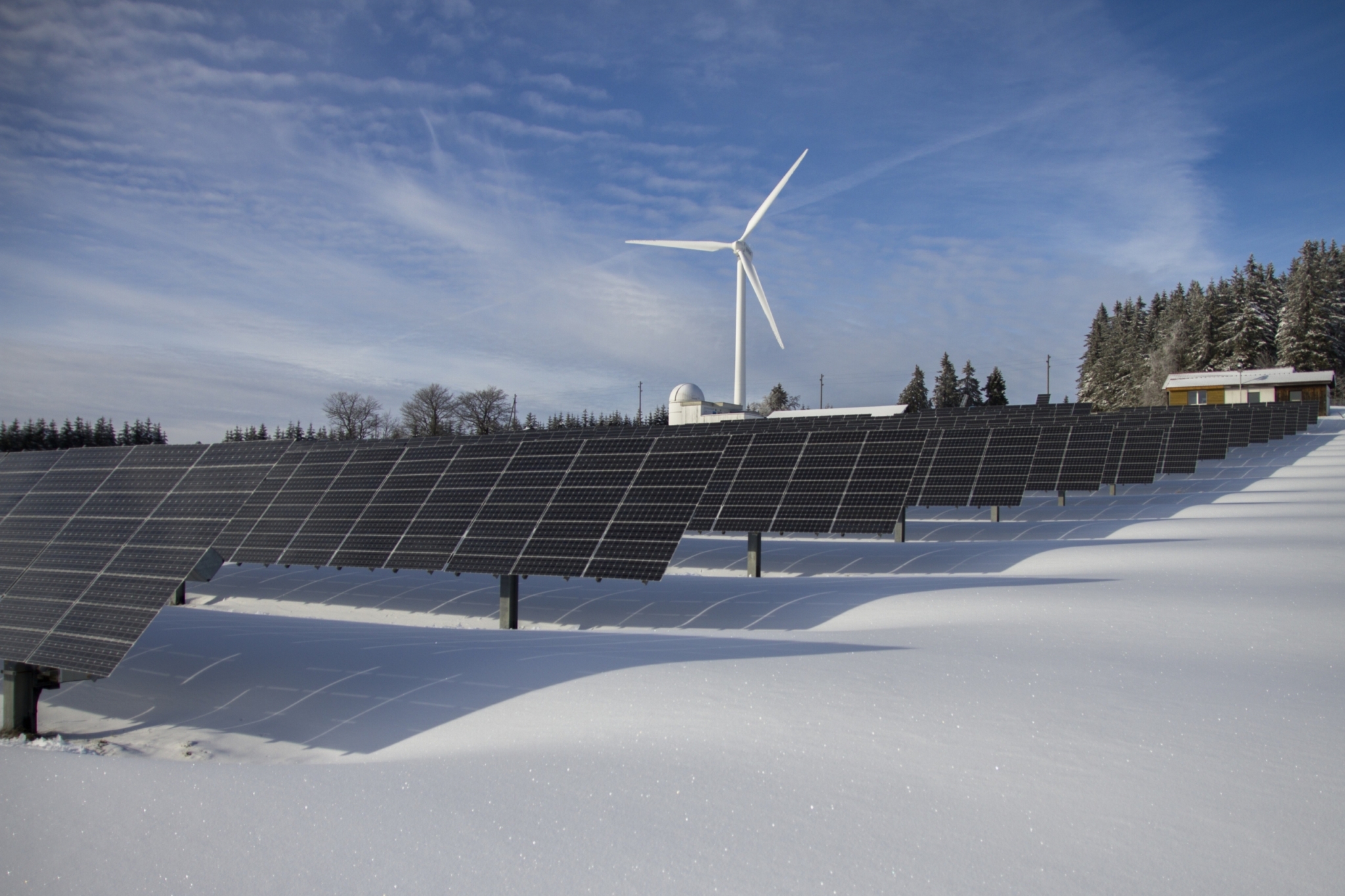 Solar panels on snow with windmill under clear day sky as a way of implementing sustainable business practices.