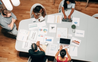 A group of people sitting around a table in an office, discussing a project related to innovation in business.